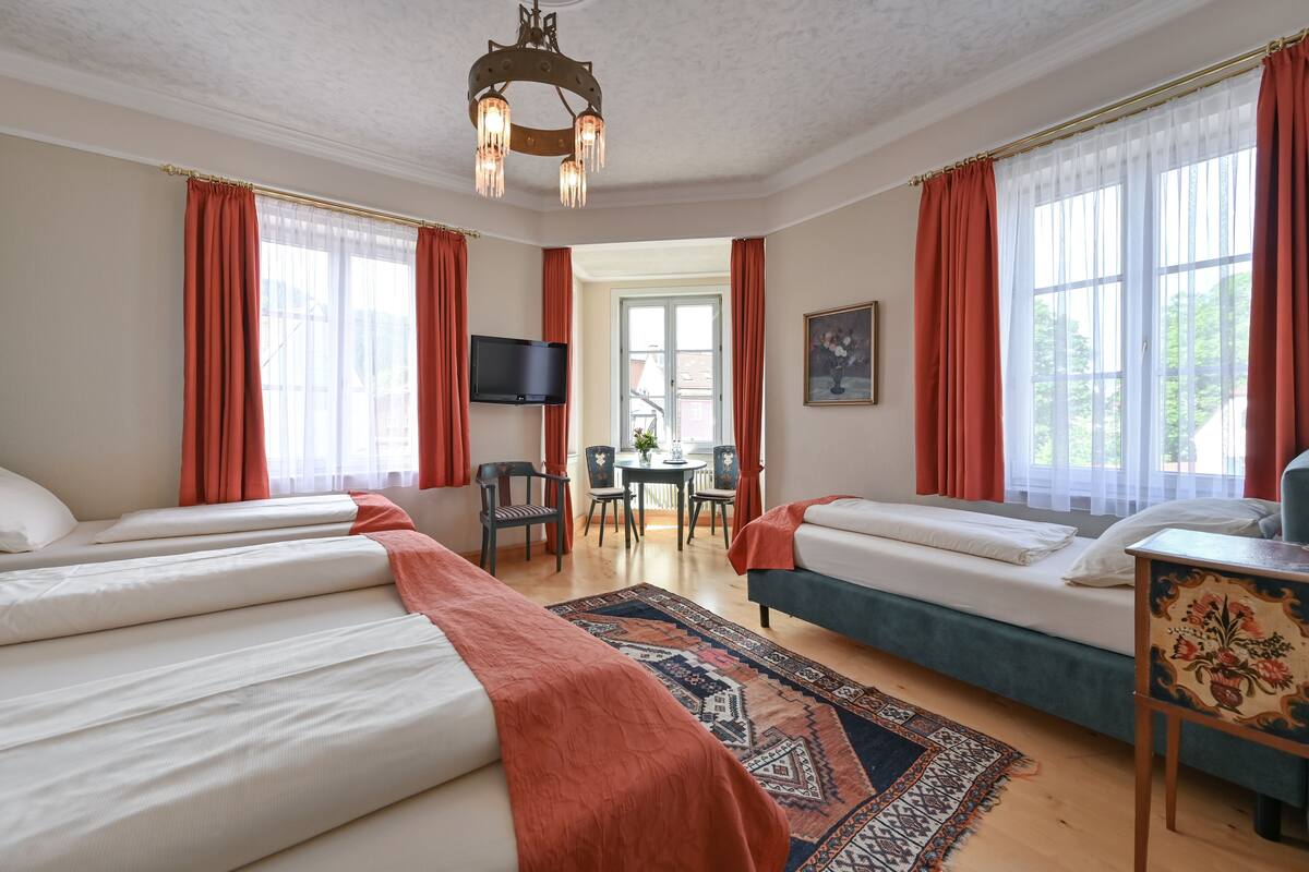 Habitación de hotel con dos camas, un escritorio, una silla, un televisor y una ventana con cortinas.