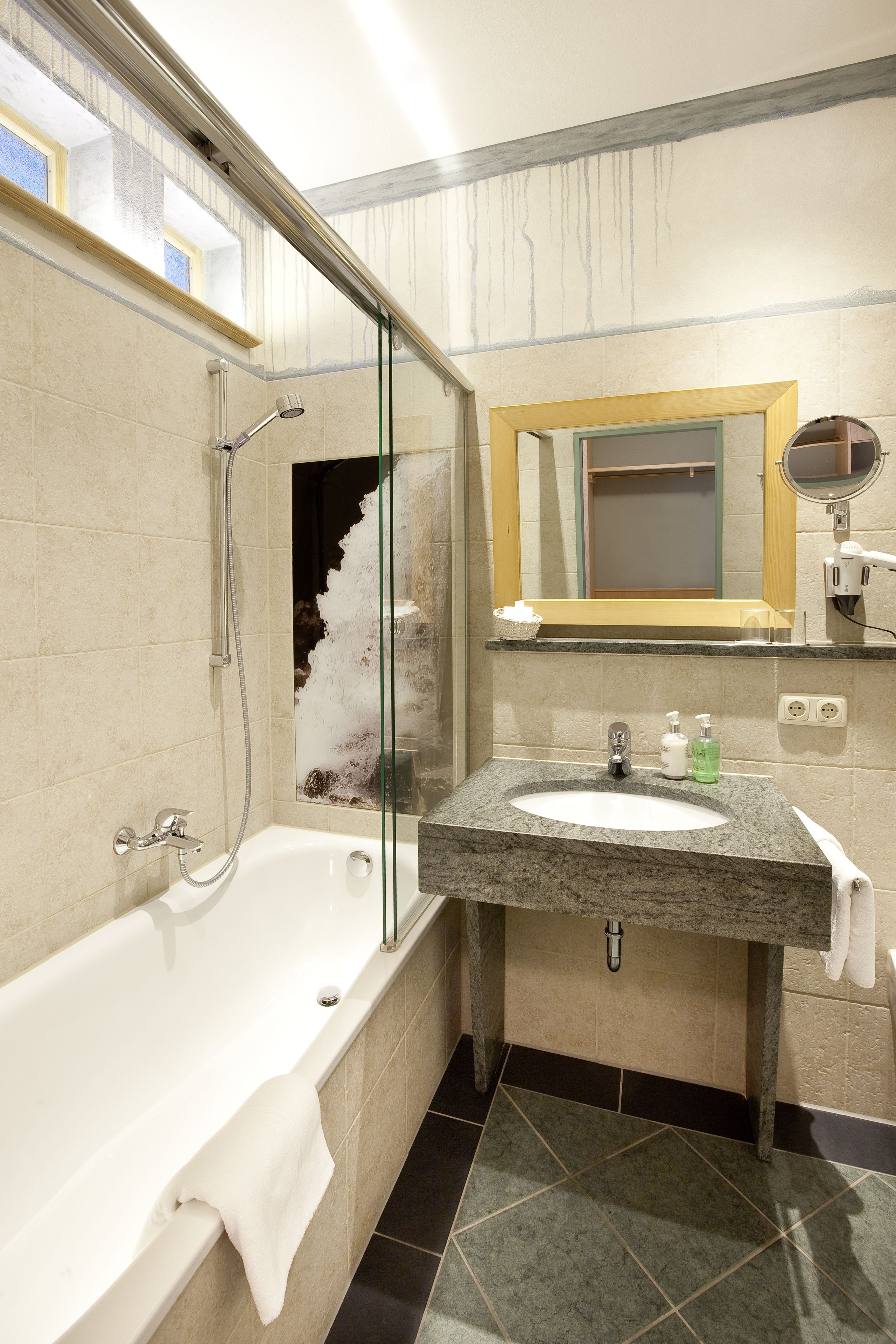 A modern bathroom with a glass-enclosed shower, a freestanding bathtub, a granite countertop sink, and a mirror above the sink.