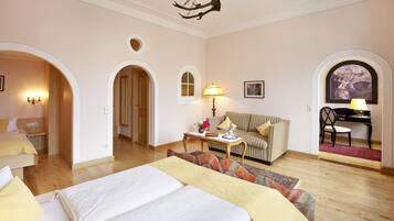 Quarto de hotel com uma cama grande, um sofá, uma escrivaninha com cadeira e um espaço de refeições com um piano.