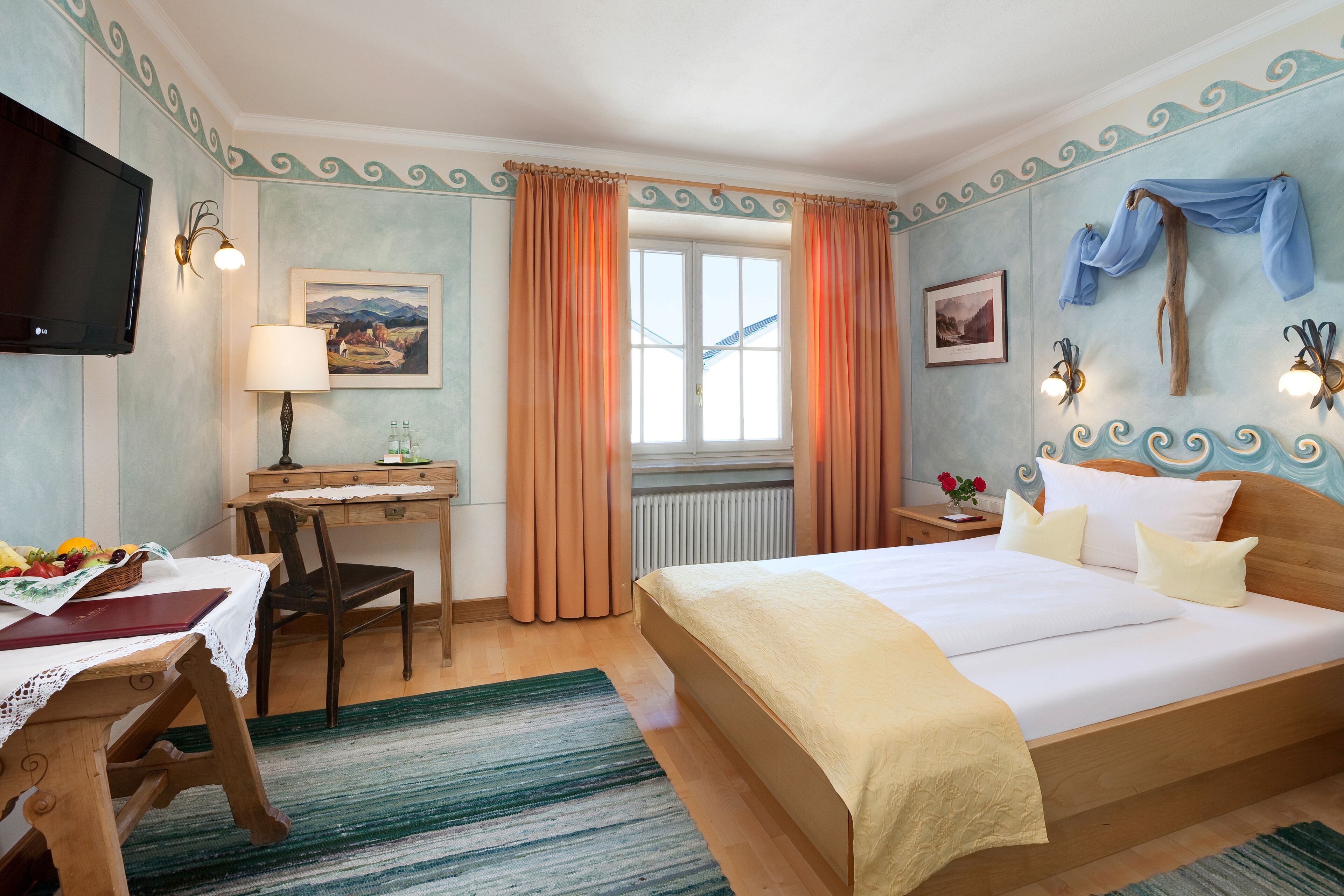 Habitación de hotel con cama, escritorio, silla, televisor y ventana con cortinas.