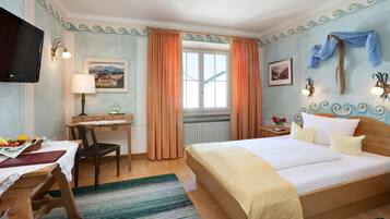 A hotel room with a bed, a desk, a chair, a television, and a window with curtains.