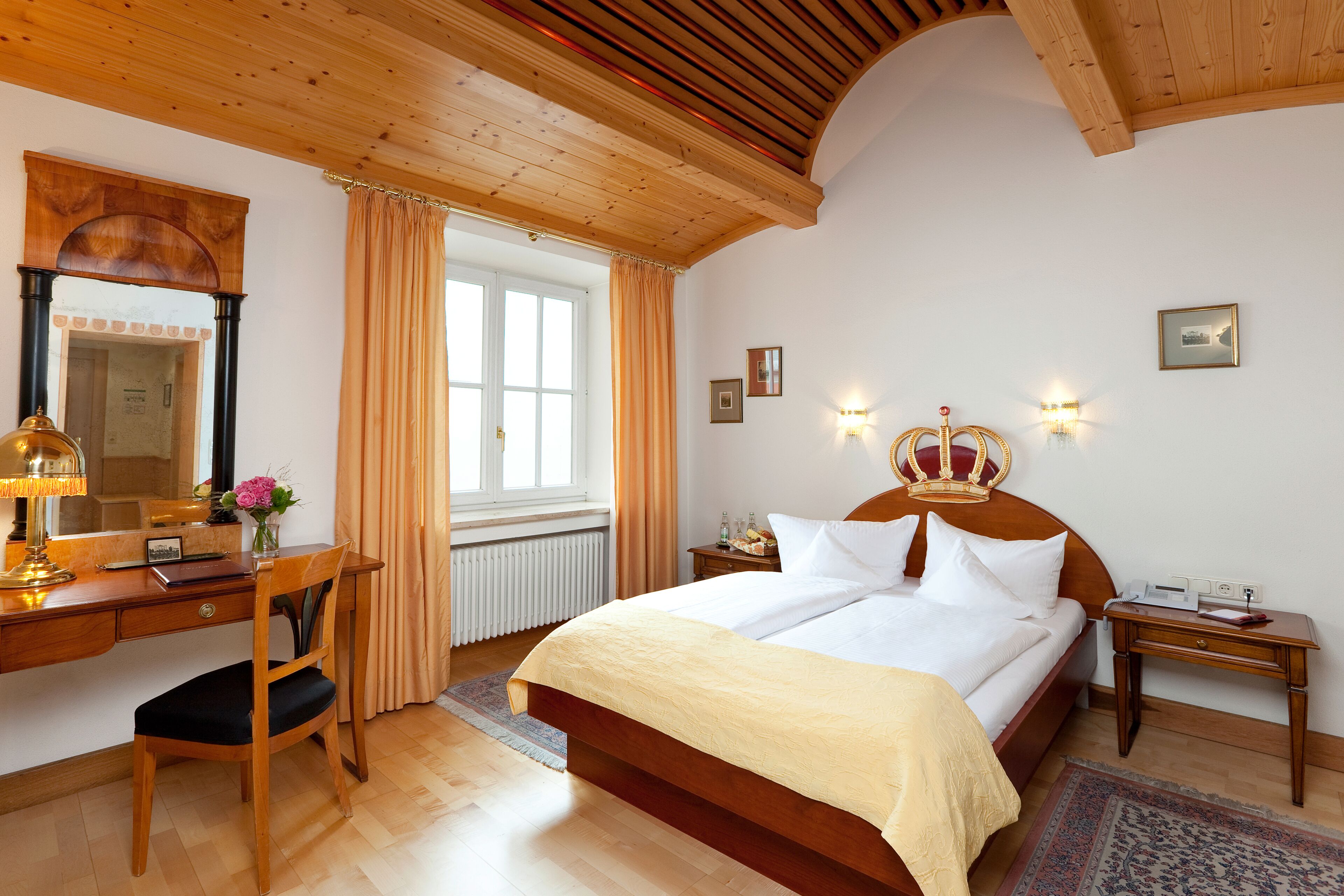 A bedroom with a wooden bed, a desk with a chair, a mirror, and a window with curtains.