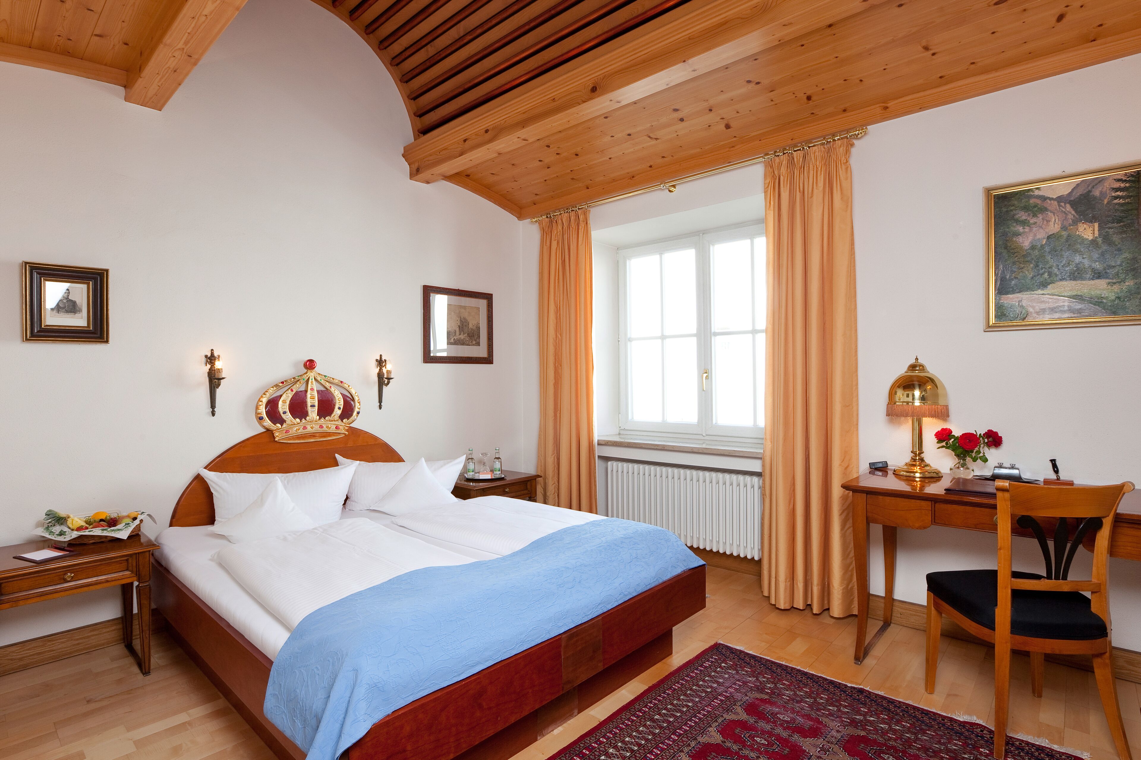 A bedroom with a wooden bed, a desk with a lamp, and a window with curtains.
