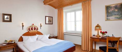 A bedroom with a wooden bed, a desk with a lamp, and a window with curtains.
