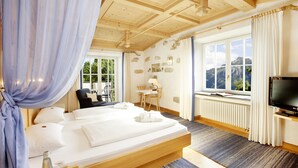 Een slaapkamer met een houten plafond, een groot bed, een televisie, een bureau en uitzicht op bergen door het raam.