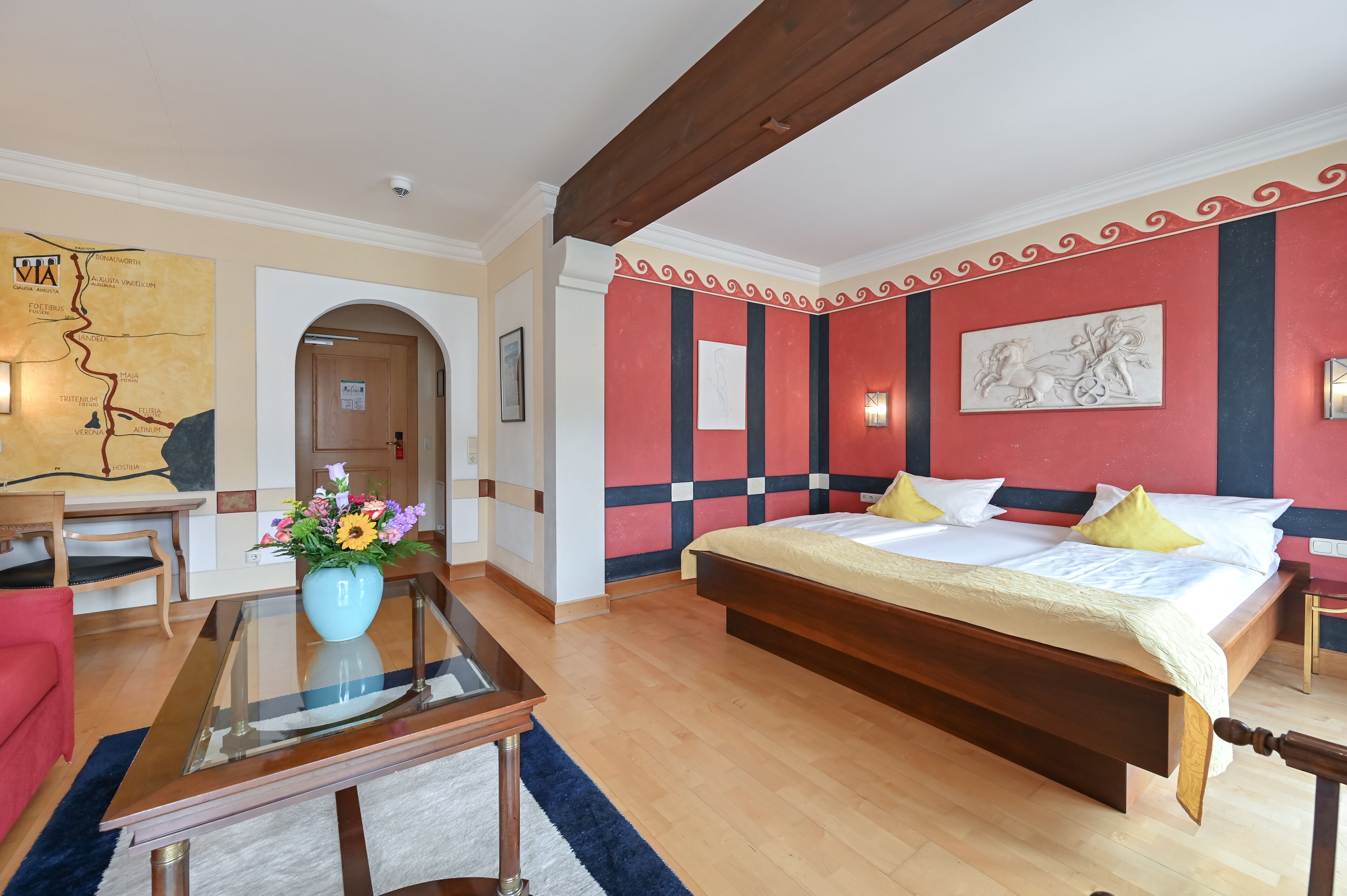 Una habitación de hotel con una cama grande, una mesa de centro de vidrio, un sofá rojo y un mapa en la pared.