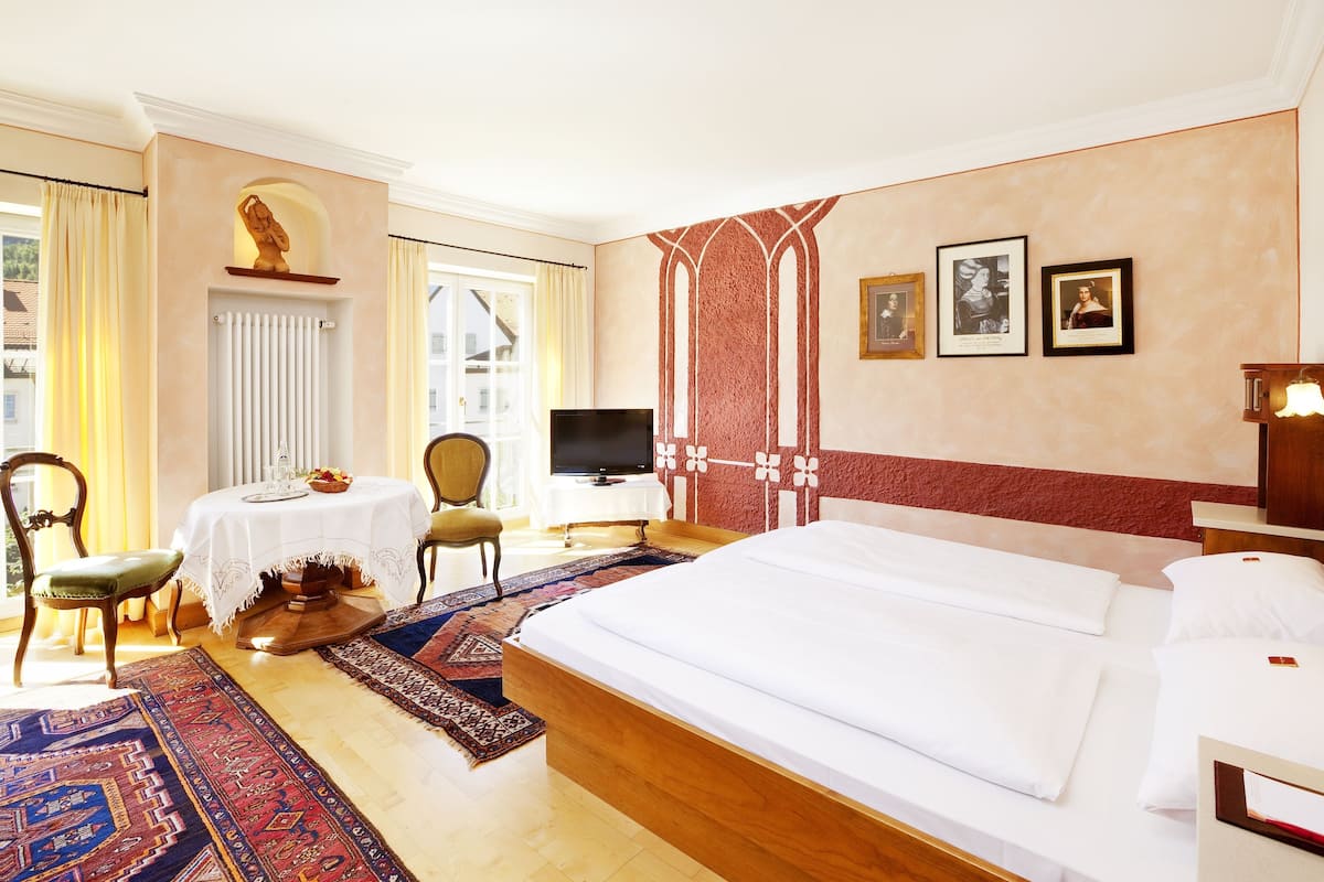 Habitación de hotel con una cama grande, televisión, escritorio con silla y ventana con cortinas.