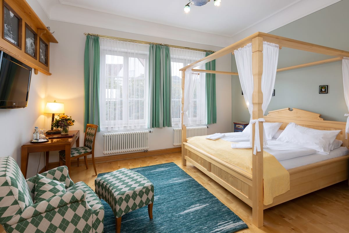Un dormitorio con una cama con dosel, un escritorio con lámpara, una silla y una pequeña mesa con un florero.