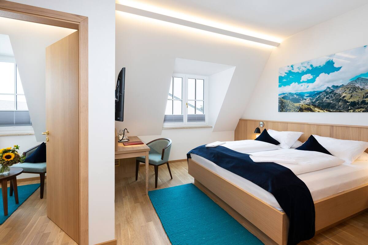 Habitación de hotel moderna con cama, escritorio, silla y un amplio ventanal.