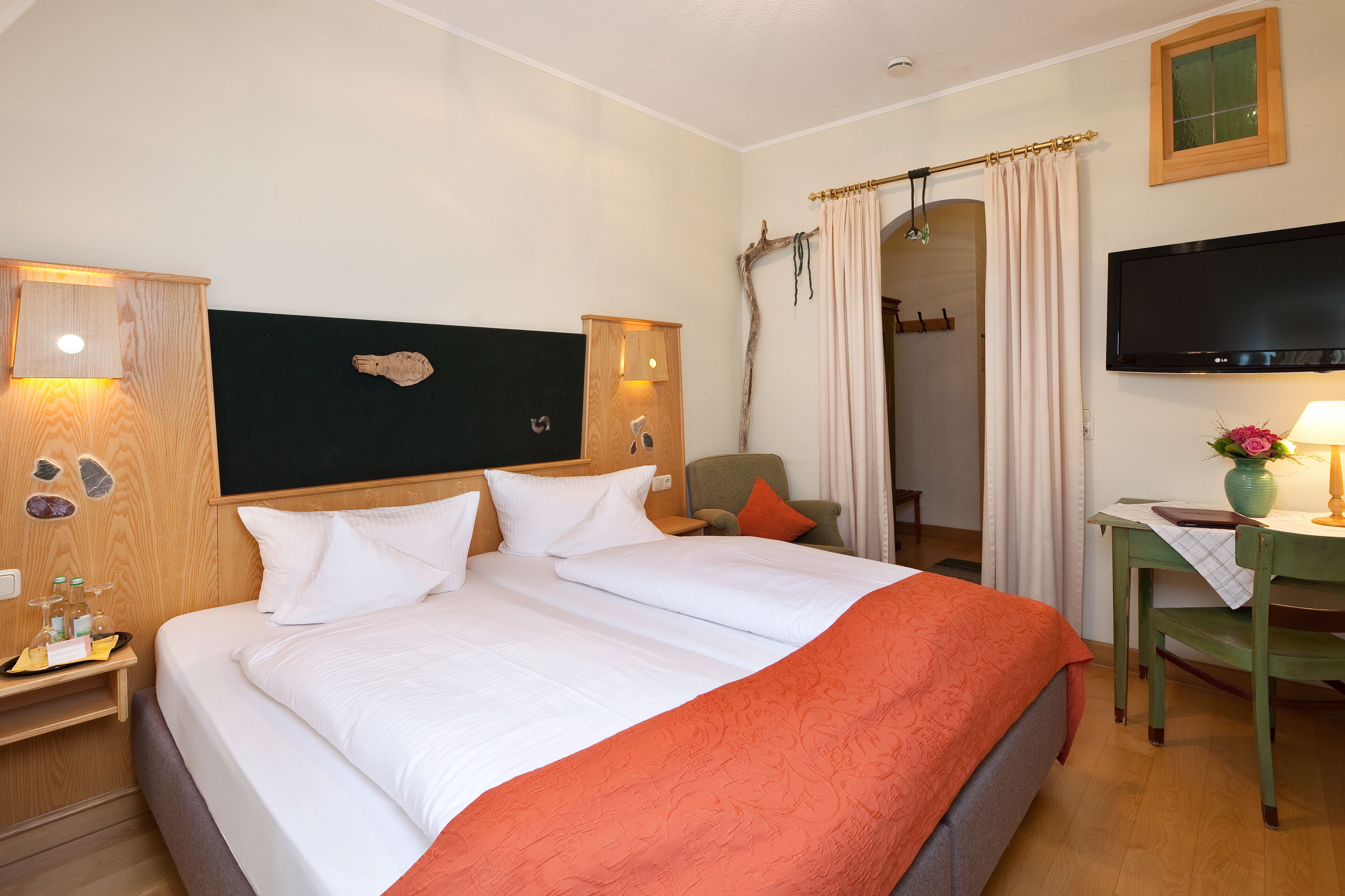 Habitación de hotel con una cama grande, un escritorio con silla, televisión y baño visible a través de un arco.