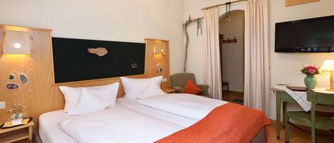 Habitación de hotel con una cama grande, un escritorio con silla, televisión y baño visible a través de un arco.