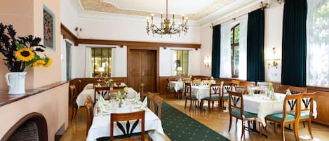 A dining area with wooden tables, chairs, and a chandelier.