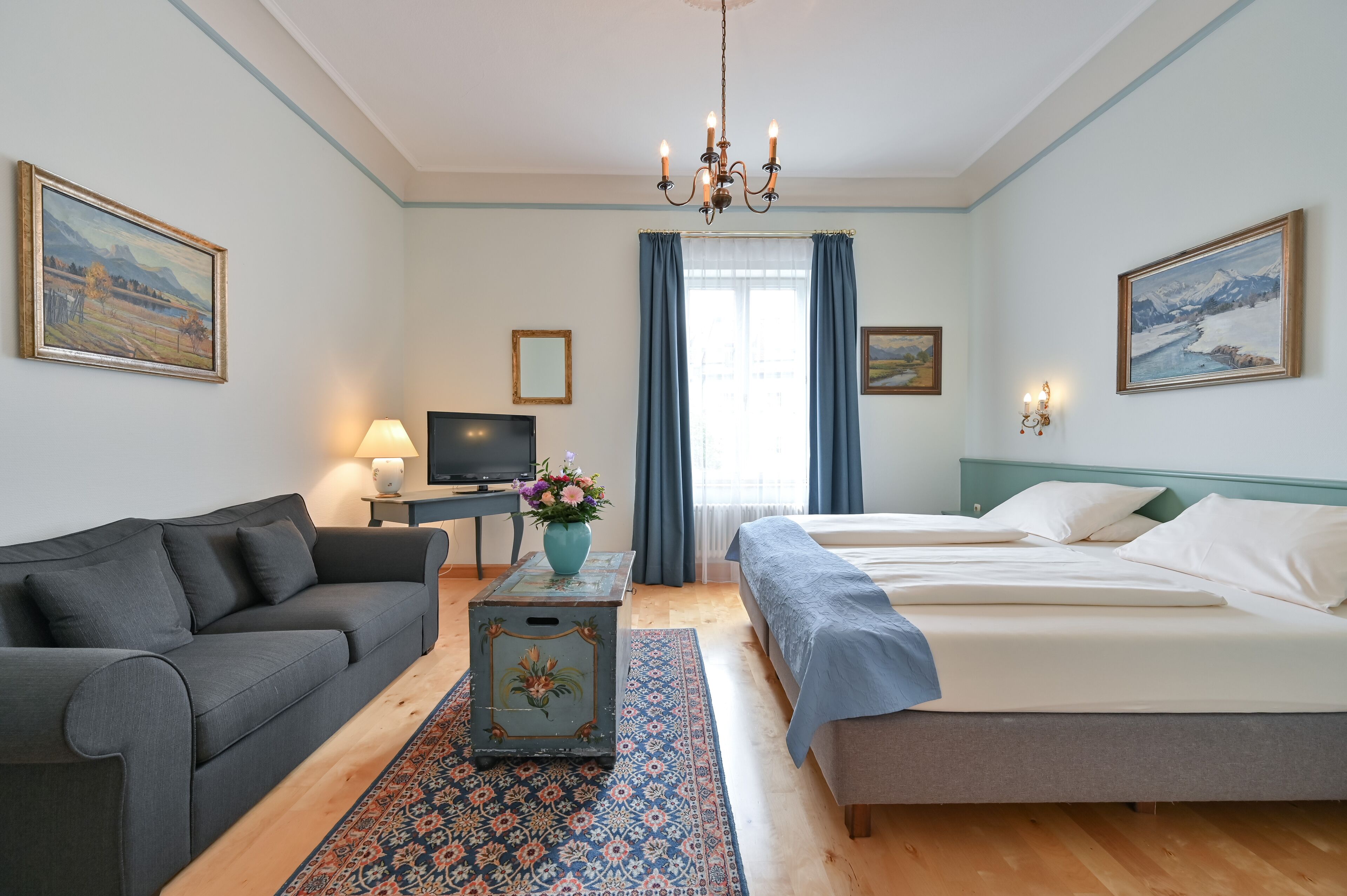 Ett hotellrum med en soffa, en säng, en tv, en lampa och en tavla på väggen.