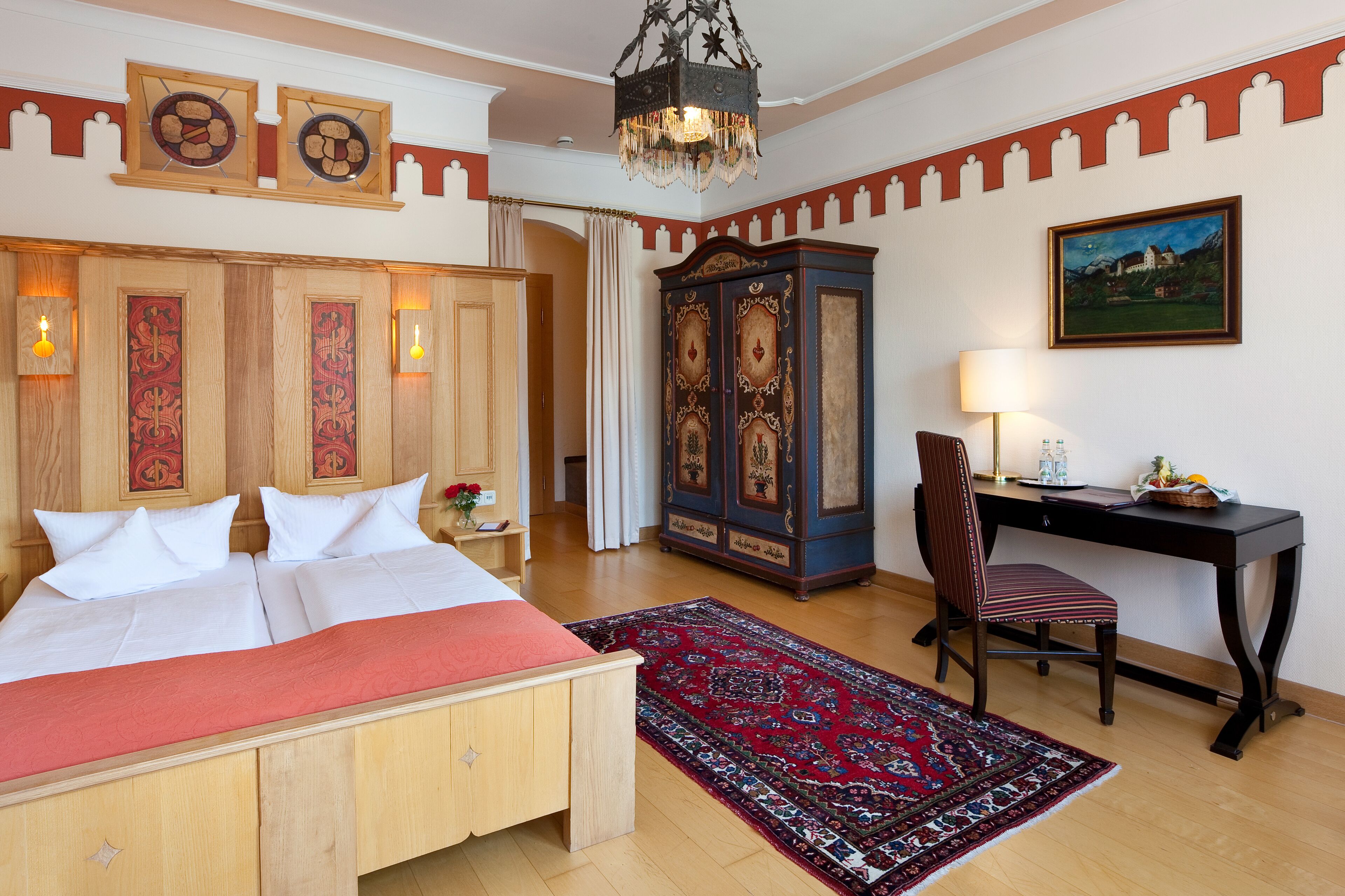 A hotel room with a large bed, a desk, a chair, a cabinet, and a painting on the wall.