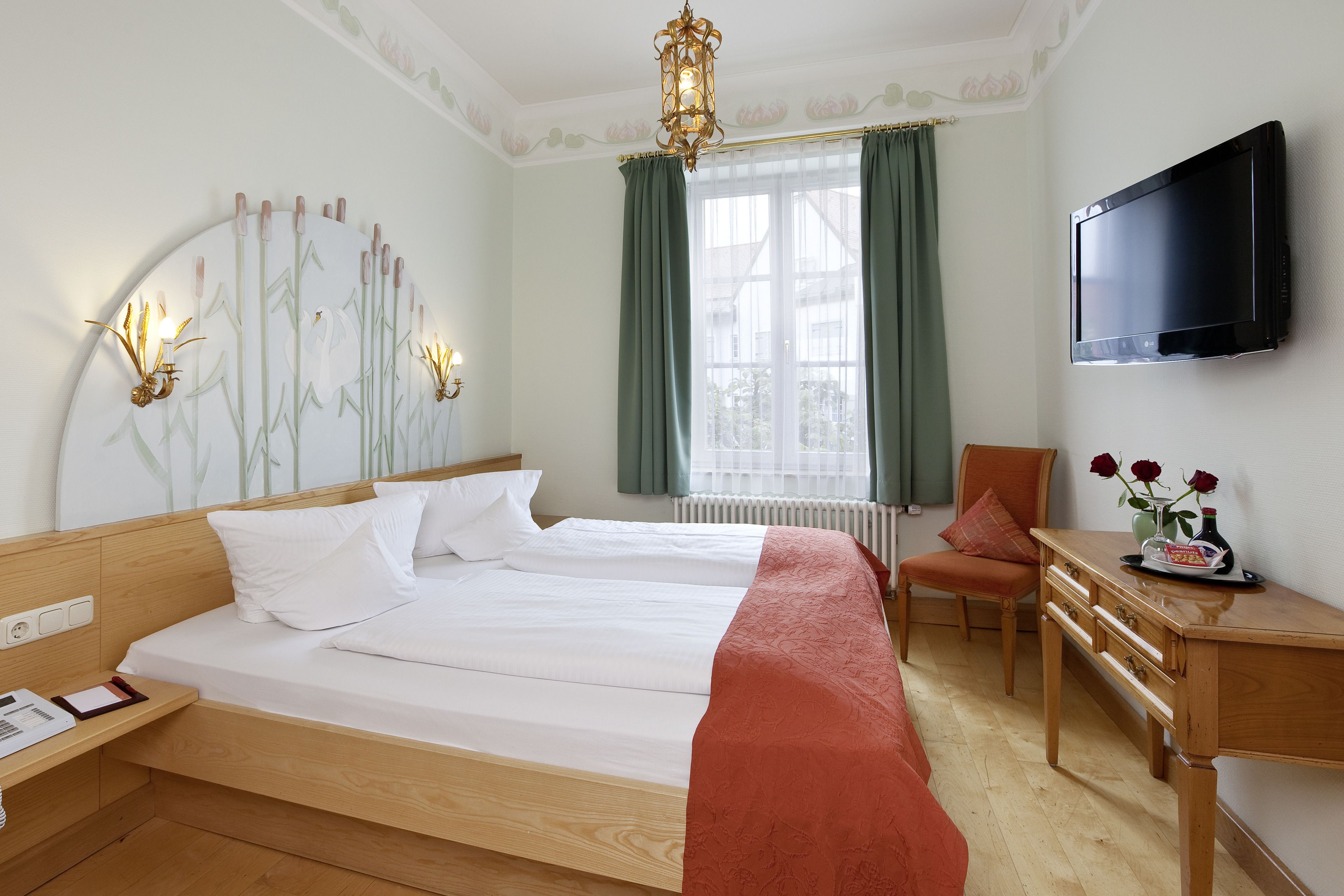 Una habitación de hotel con una cama grande, un escritorio, una silla, un televisor y una ventana con cortinas.