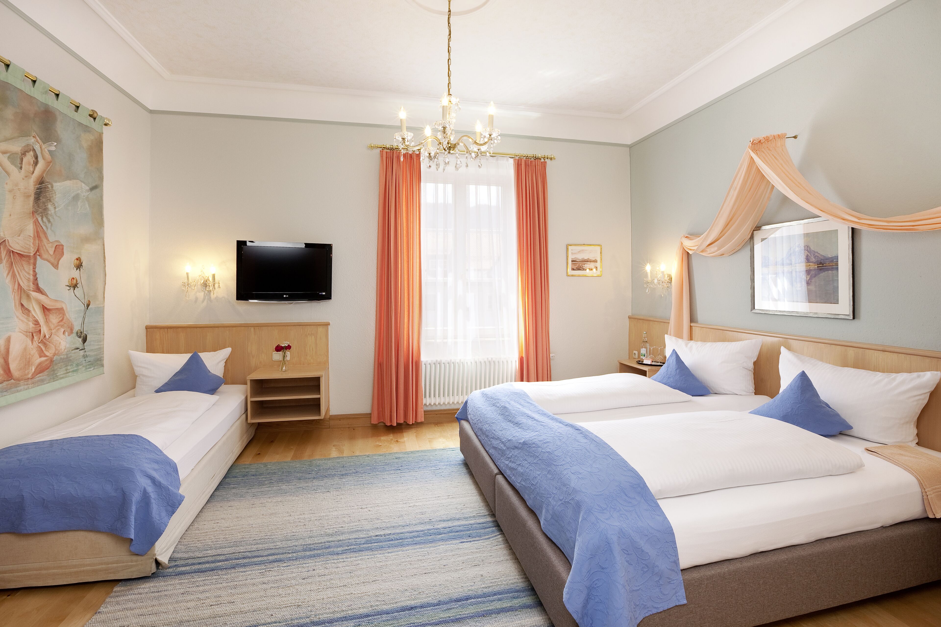 A hotel room with two beds, a television, a chandelier, and a large painting on the wall.
