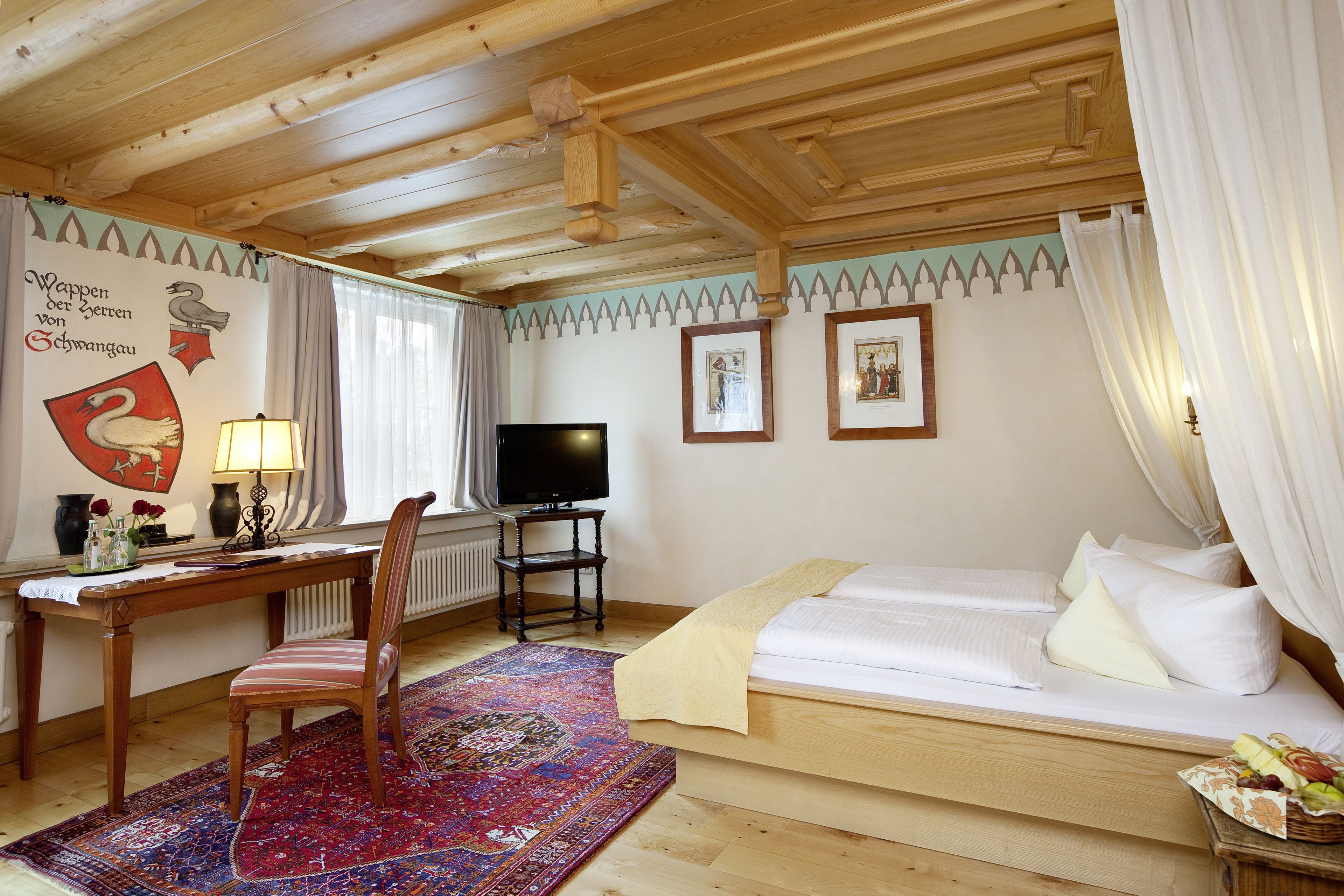A wooden room with a bed, a desk, a chair, a TV, and a wall with framed pictures.