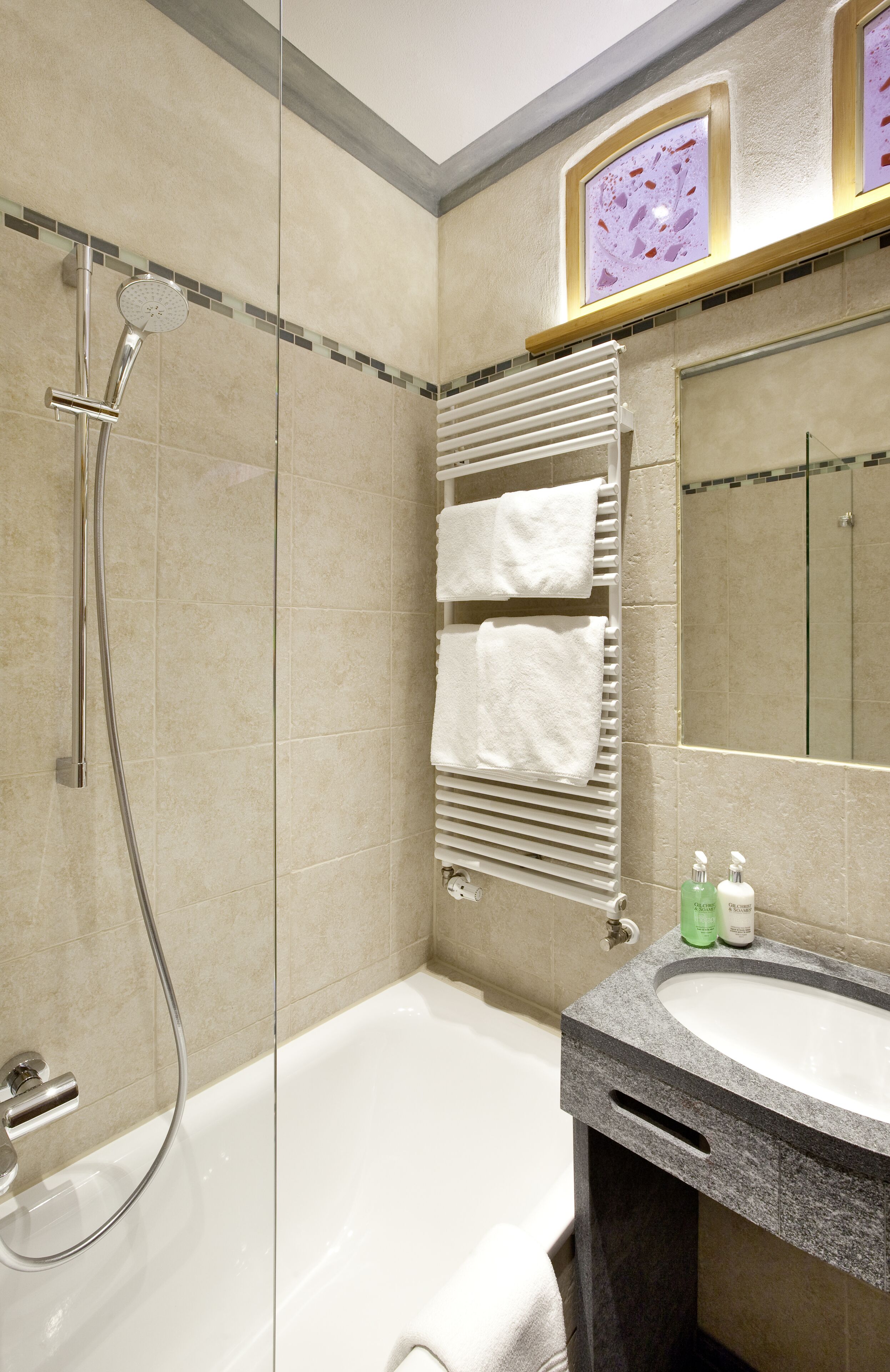 Un baño con bañera, ducha, toallero y lavamanos con artículos de aseo.