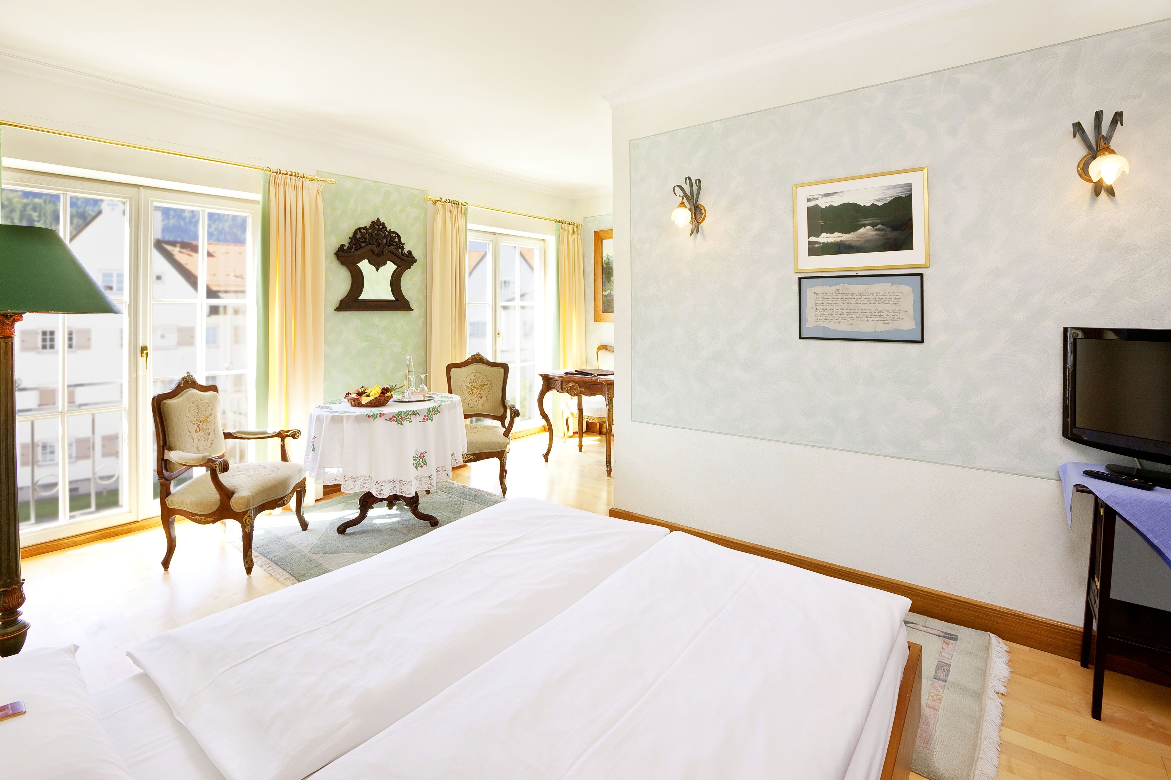 A hotel room with a large bed, a television, a desk with a chair, and a window with curtains.