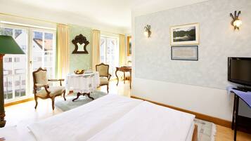 A hotel room with a large bed, a television, a desk with a chair, and a window with curtains.