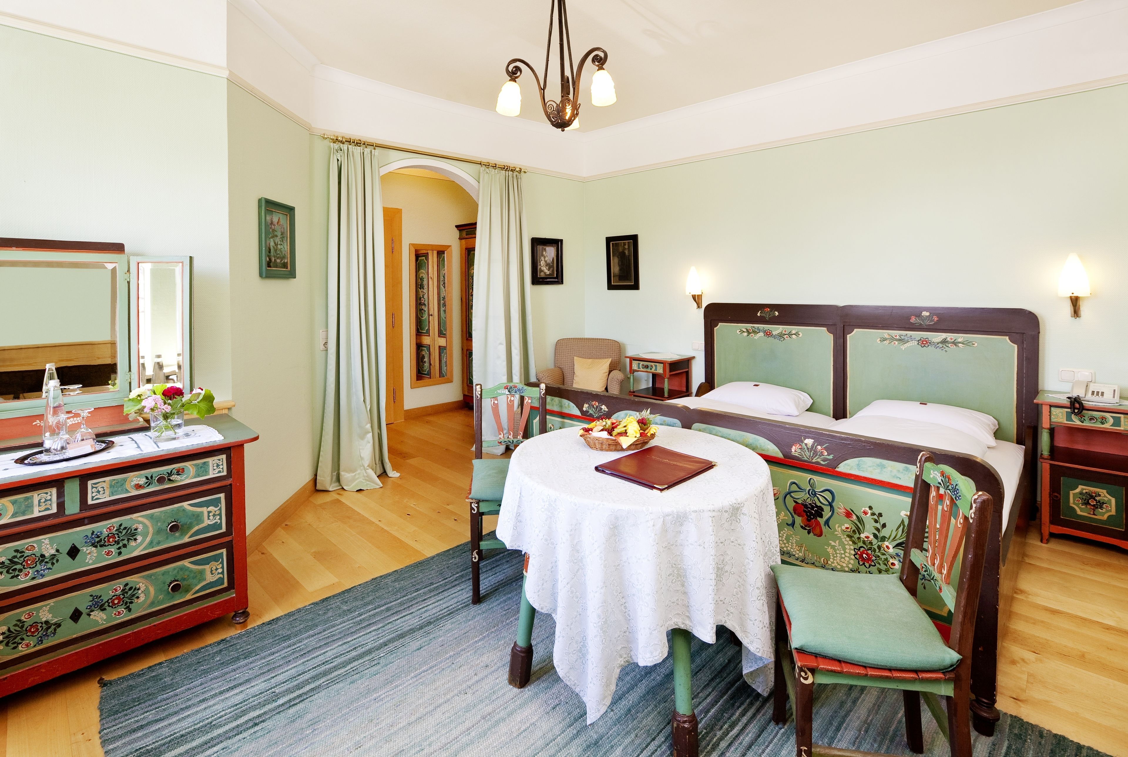 Quarto com cama, cômoda, cadeira, mesa e lustre.