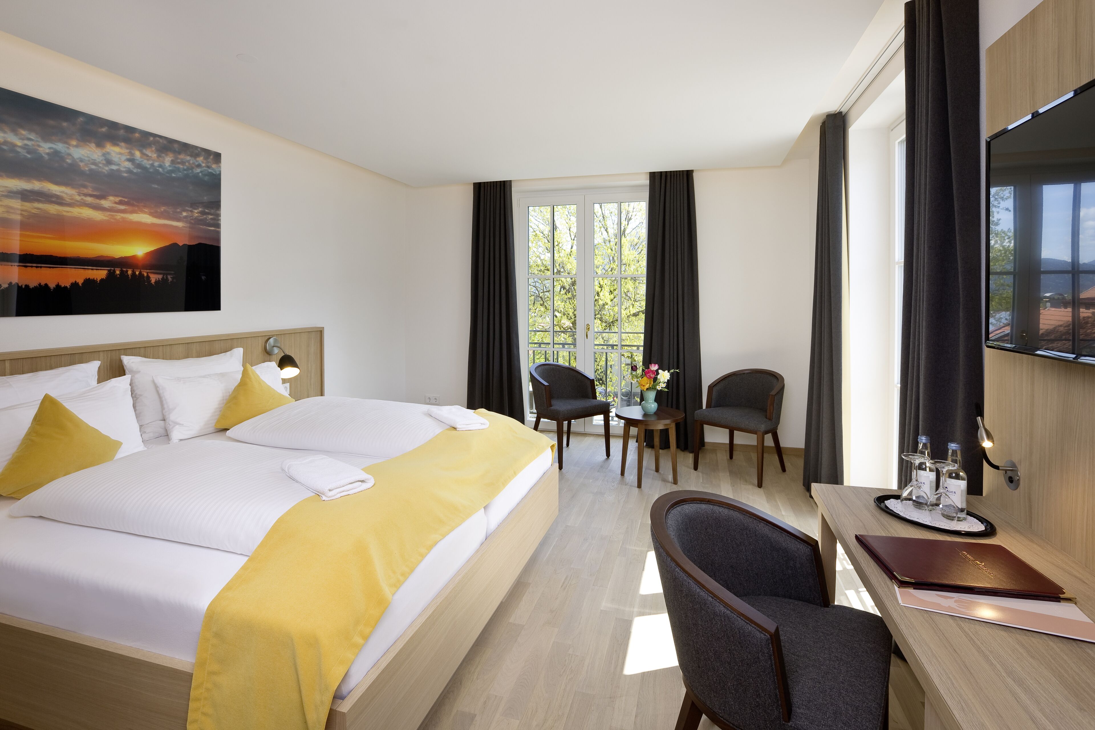 Una habitación de hotel con cama, escritorio, dos sillas, televisor y ventana con cortinas.