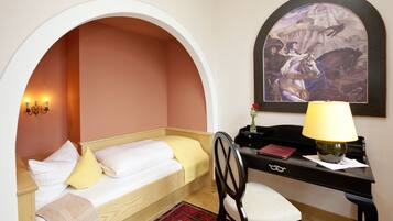 A bedroom with a single bed, a desk, a chair, a lamp, and a painting on the wall.