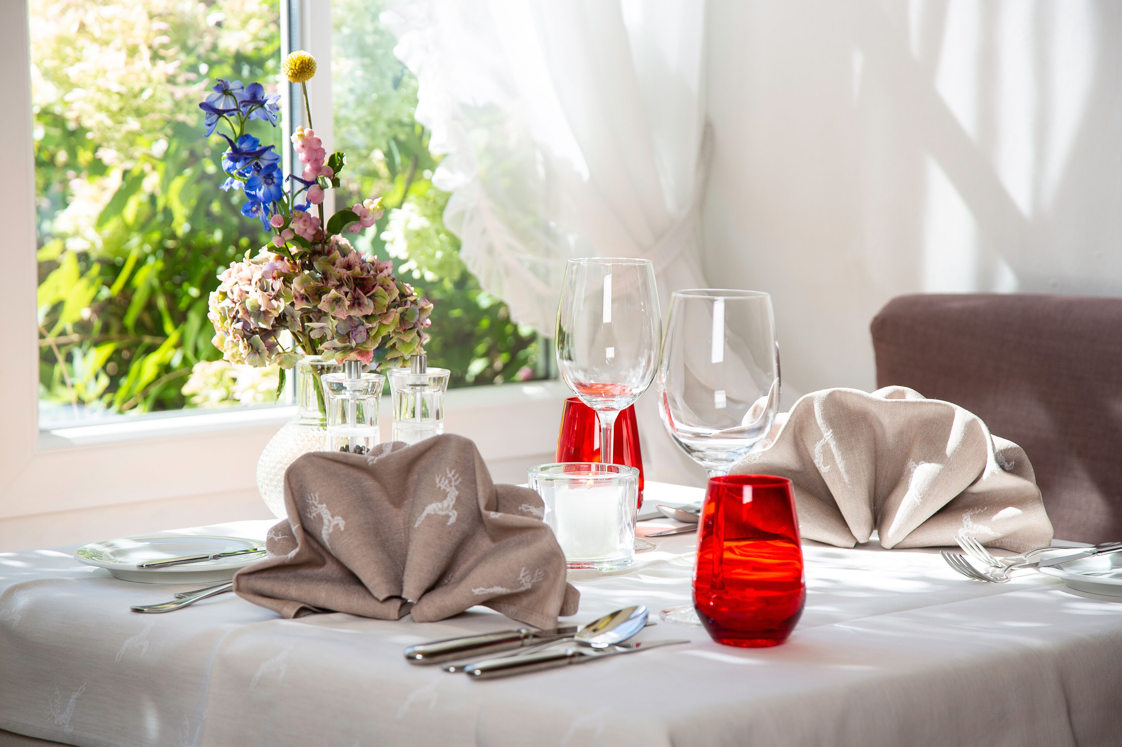 A table set for two with a vase of flowers, wine glasses, and a candle.