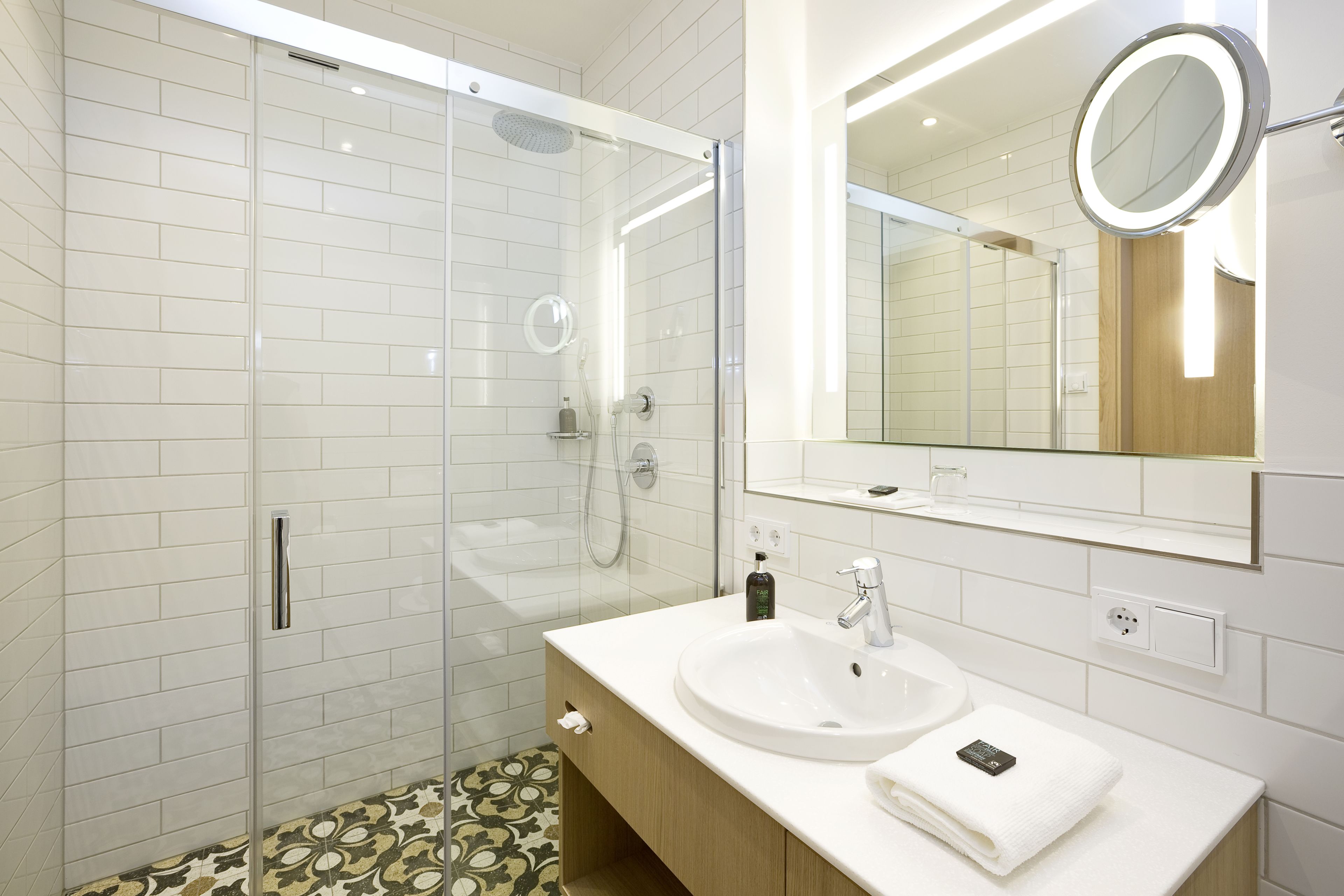 A modern bathroom with a glass-enclosed shower, a white sink, and a mirror with a round frame.
