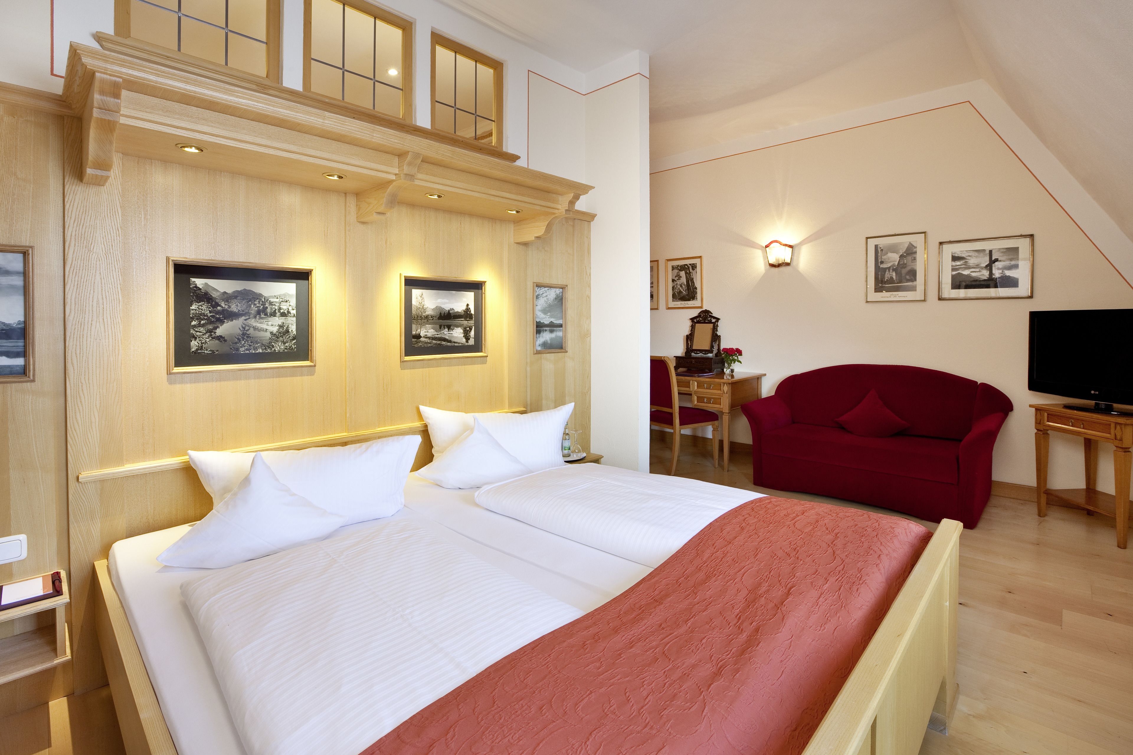 Ein Hotelzimmer mit einem großen Bett, einem roten Sessel, einem Schreibtisch mit Stuhl und einem Fernseher.