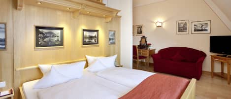 A hotel room with a large bed, a red armchair, a desk with a chair, and a television.