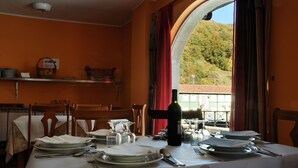 A dining table set with plates, glasses, and cutlery, a bottle of wine, and a view of a mountainous landscape through an arched window.