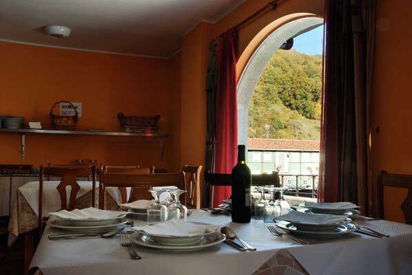 A dining table set with plates, glasses, and cutlery, a bottle of wine, and a view of a mountainous landscape through an arched window.