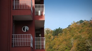 A red building with balconies and a view of a forested hillside.