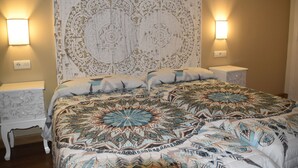 A bedroom with a large bed, patterned headboard, two bedside tables, and wall-mounted lamps.