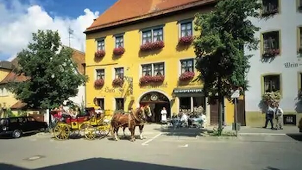 A yellow building with red flower boxes on the windows, a horse-drawn carriage, and a clear blue sky.