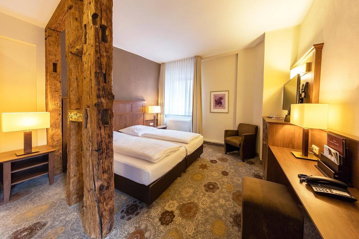 A hotel room with a large bed, a desk with a telephone, a chair, and a television.