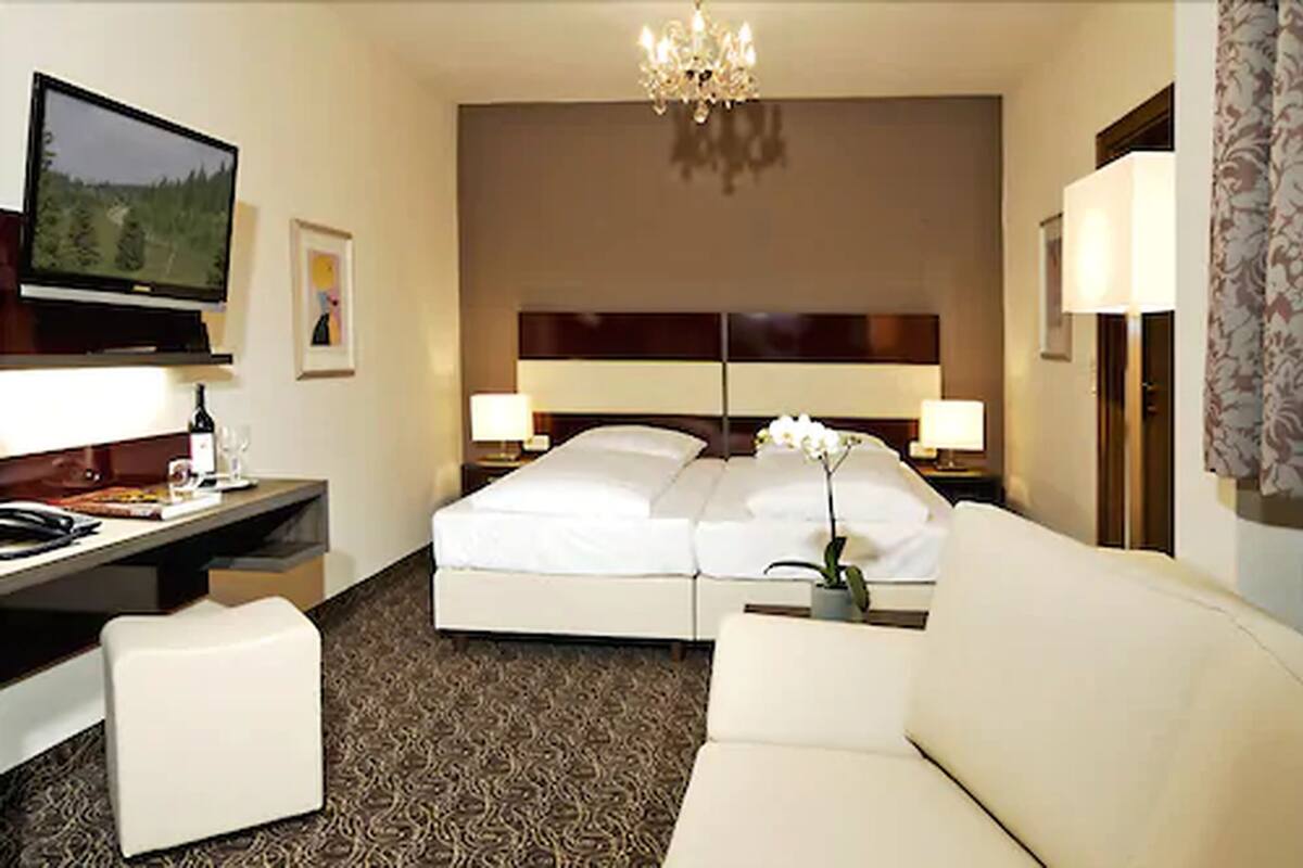 A hotel room with a bed, a desk, a television, a chandelier, and a sofa.