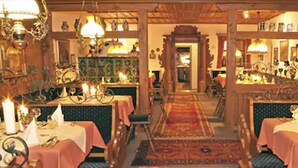 A restaurant with multiple tables, each covered with a pink tablecloth, and candle-lit chandeliers.