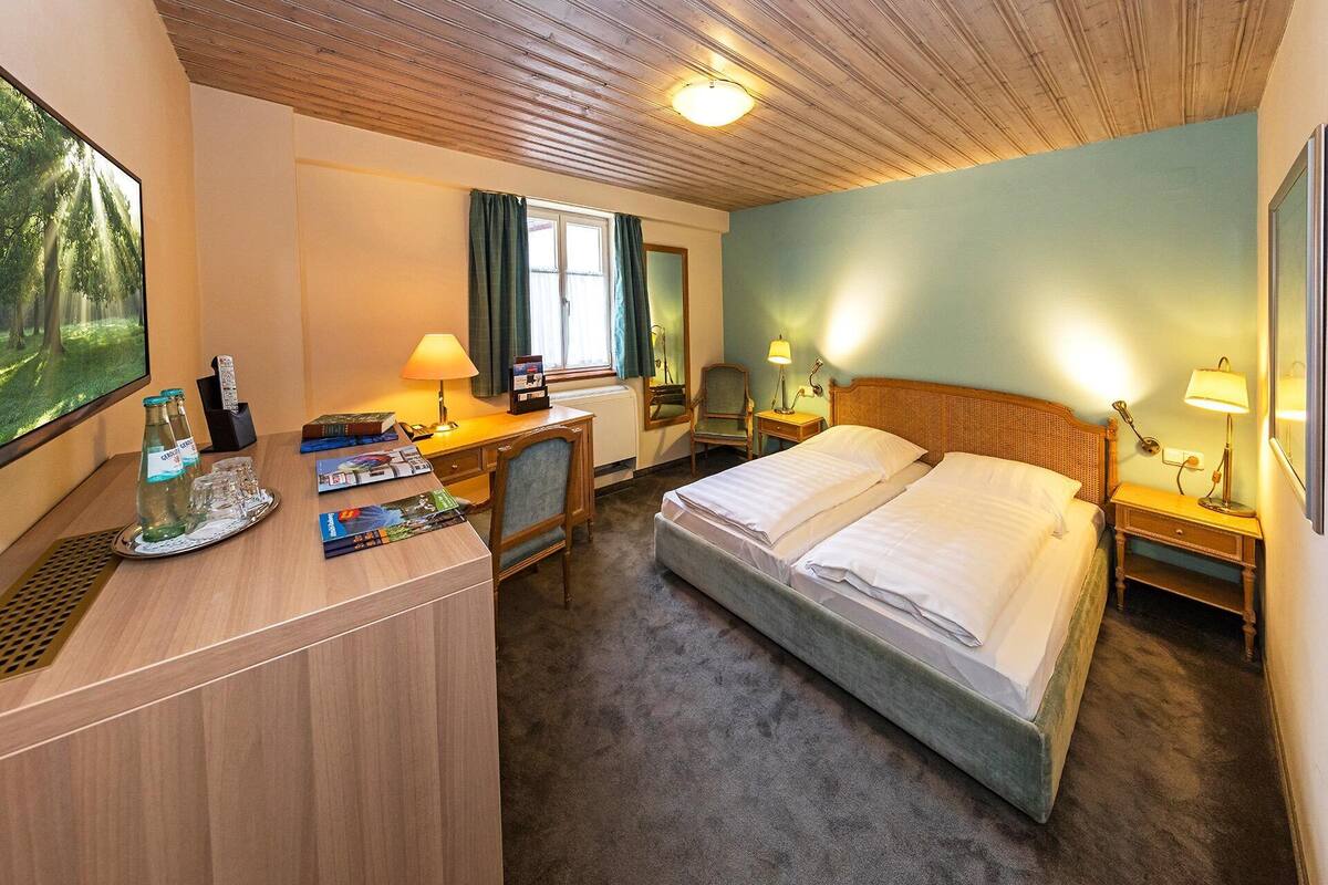 A hotel room with a bed, desk, chair, and a large window.