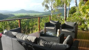 Uma varanda com móveis de vime, uma mesa de vidro e vista para uma paisagem verde.