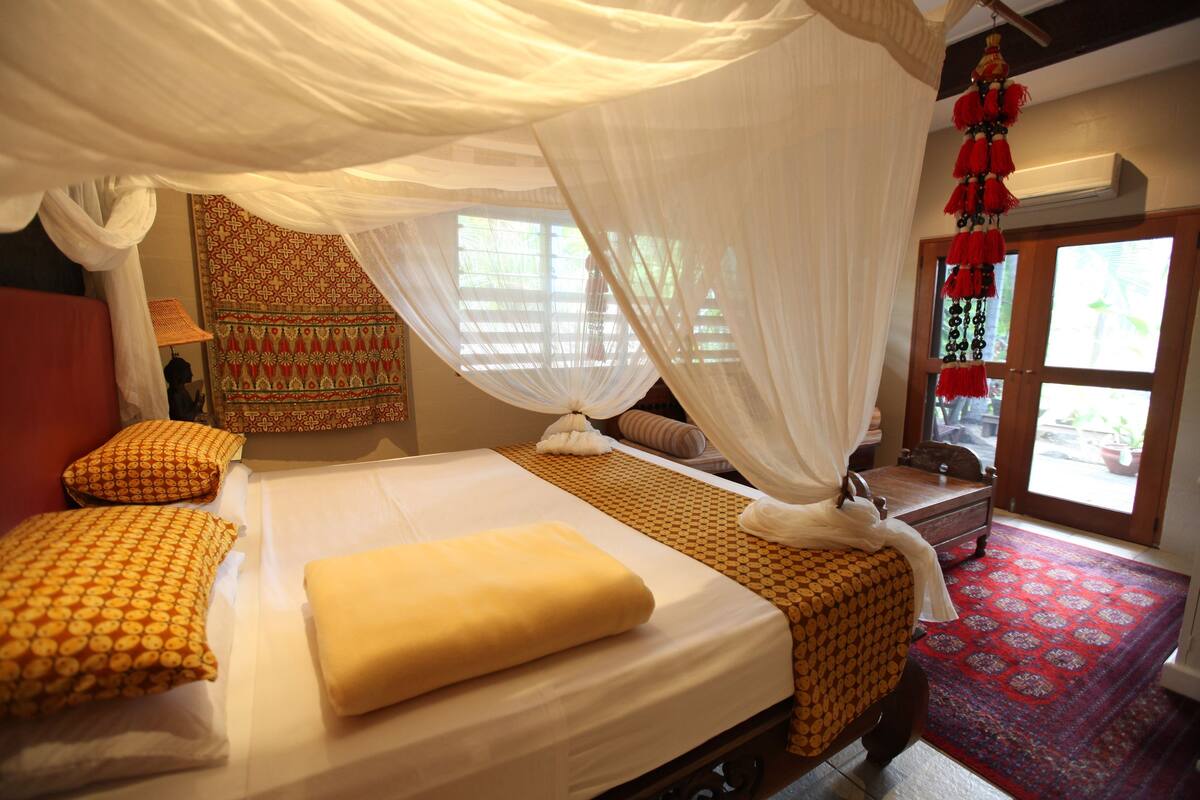 A room with a bed, a nightstand, a window with a view, and a patterned wall hanging.