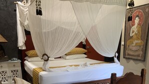 Uma cama com dossel, uma mesinha de cabeceira, uma cadeira e uma parede com um quadro.