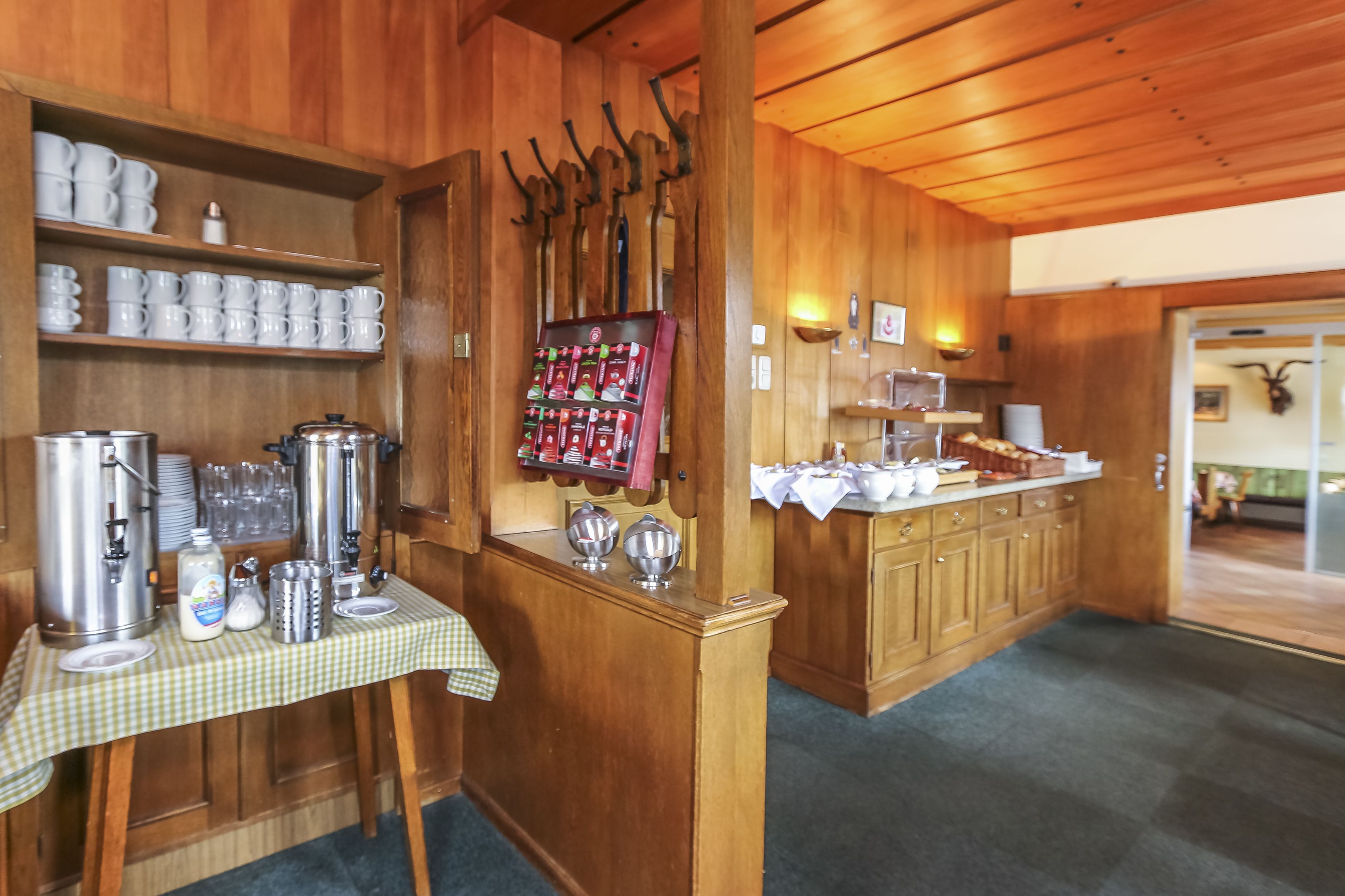 A wooden interior with a buffet setup including a coffee station, a beverage dispenser, and a variety of food items on a counter.