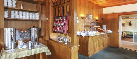 A wooden interior with a buffet setup including a coffee station, a beverage dispenser, and a variety of food items on a counter.