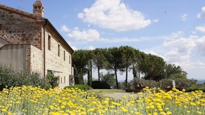 A historic building with a stone facade, surrounded by a well-maintained garden with yellow flowers and tall trees. - Antico Casale L'Impostino (Civitella Paganico)