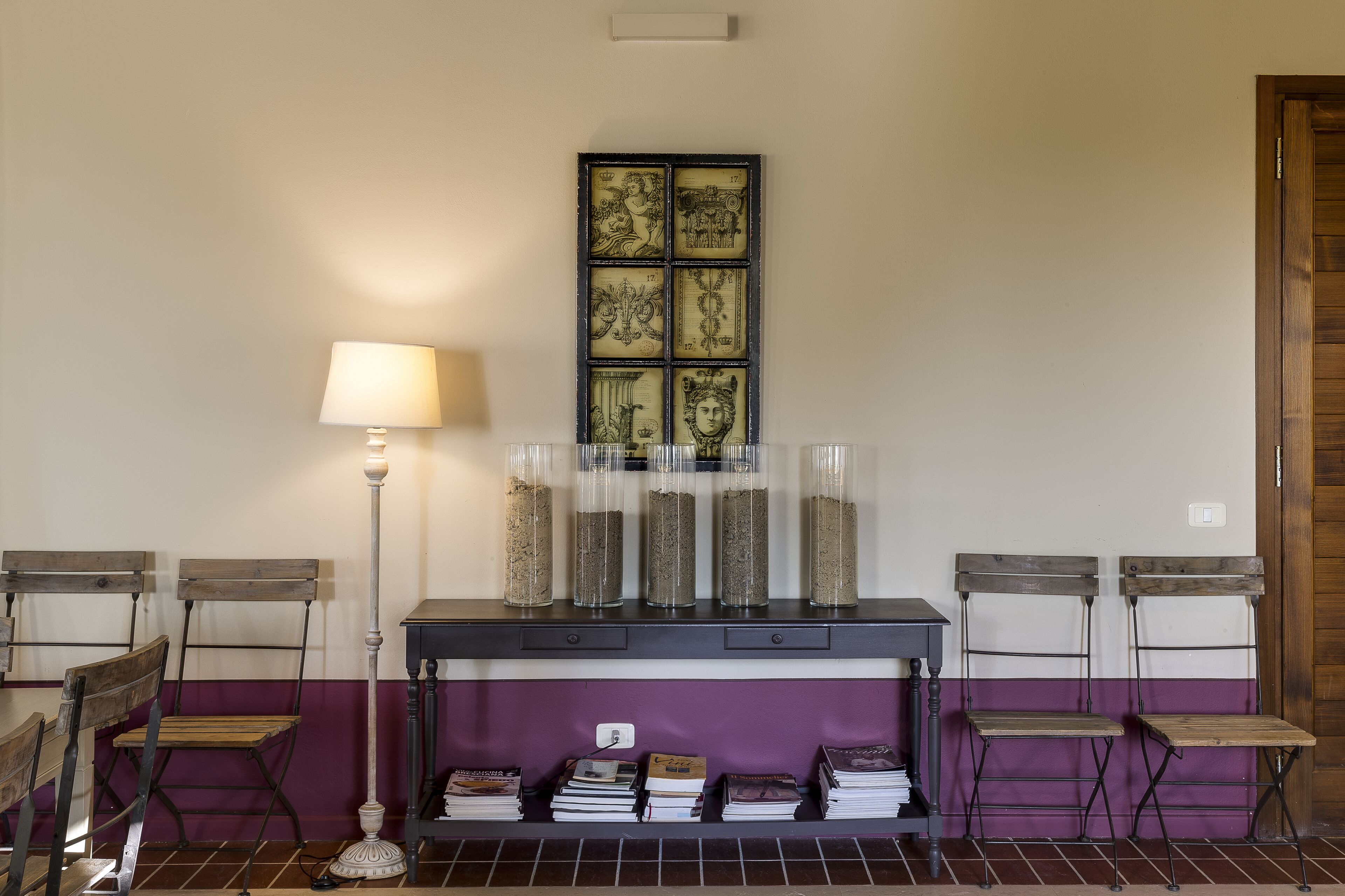 A room with a wooden table, two chairs, a lamp, and a wall-mounted display case with decorative items.