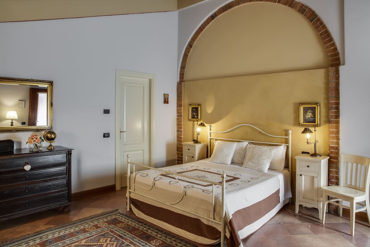 A bedroom with a bed, dresser, chair, and a large arched doorway.