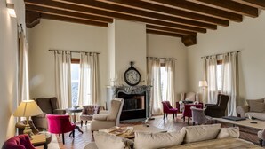 A spacious living room with a fireplace, multiple seating options, and large windows with curtains. - Antico Casale L'Impostino (Civitella Paganico)