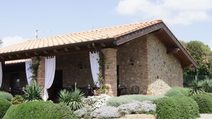 A rustic stone building with a tiled roof, a covered patio with outdoor seating, and well-maintained gardens. - Antico Casale L'Impostino (Civitella Paganico)